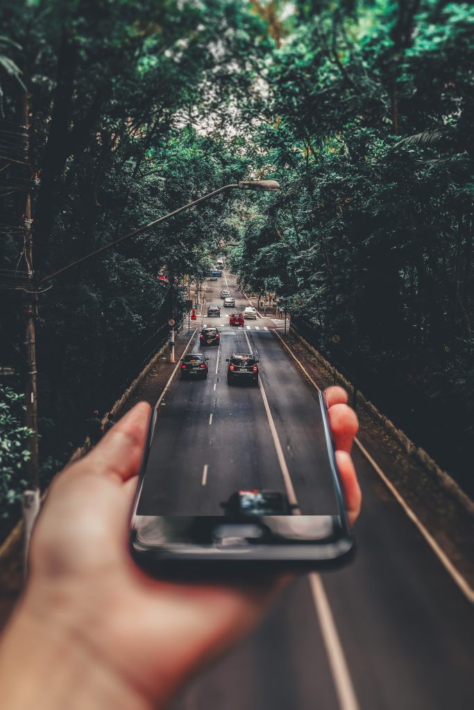 Forced perspective photography of cars running on road below smartphone