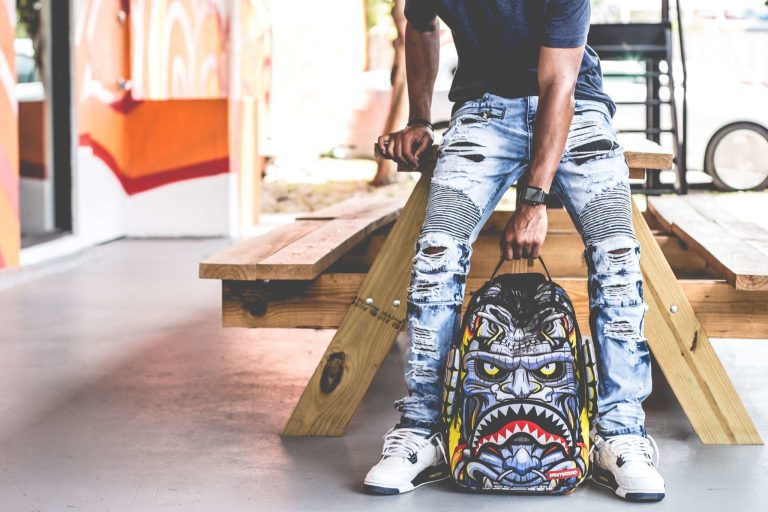 Man wearing distressed denim pants holding multicolored backpack